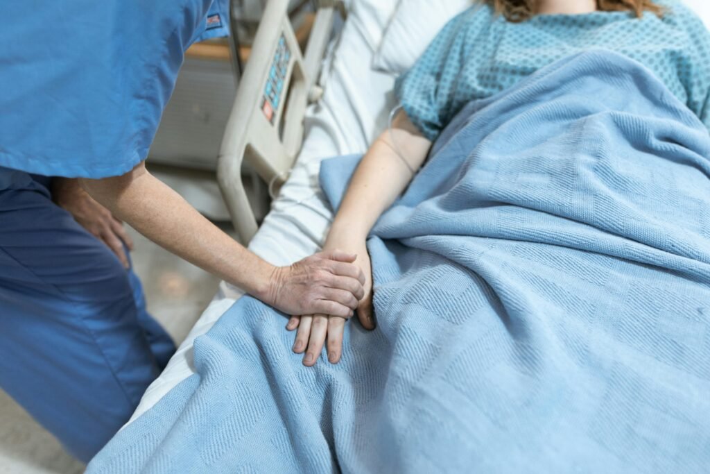 pexels-photo-6129685-6129685 A nurse in scrubs offers comfort by holding a patient's hand in a hospital bed.