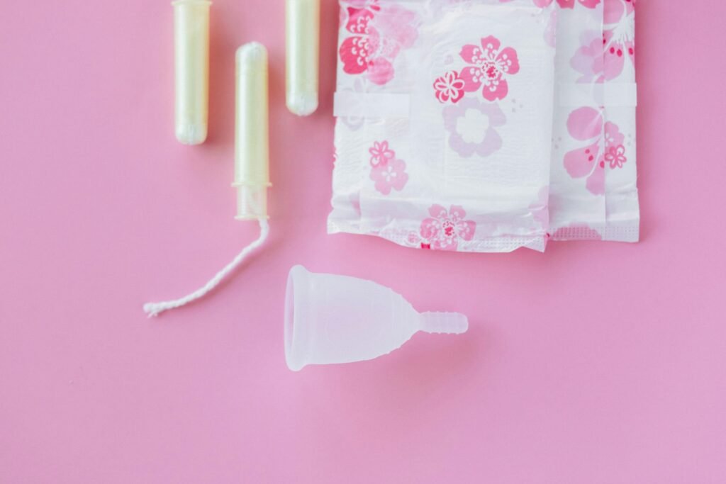 Top view of menstrual cup, pads, and tampons on a pink background.