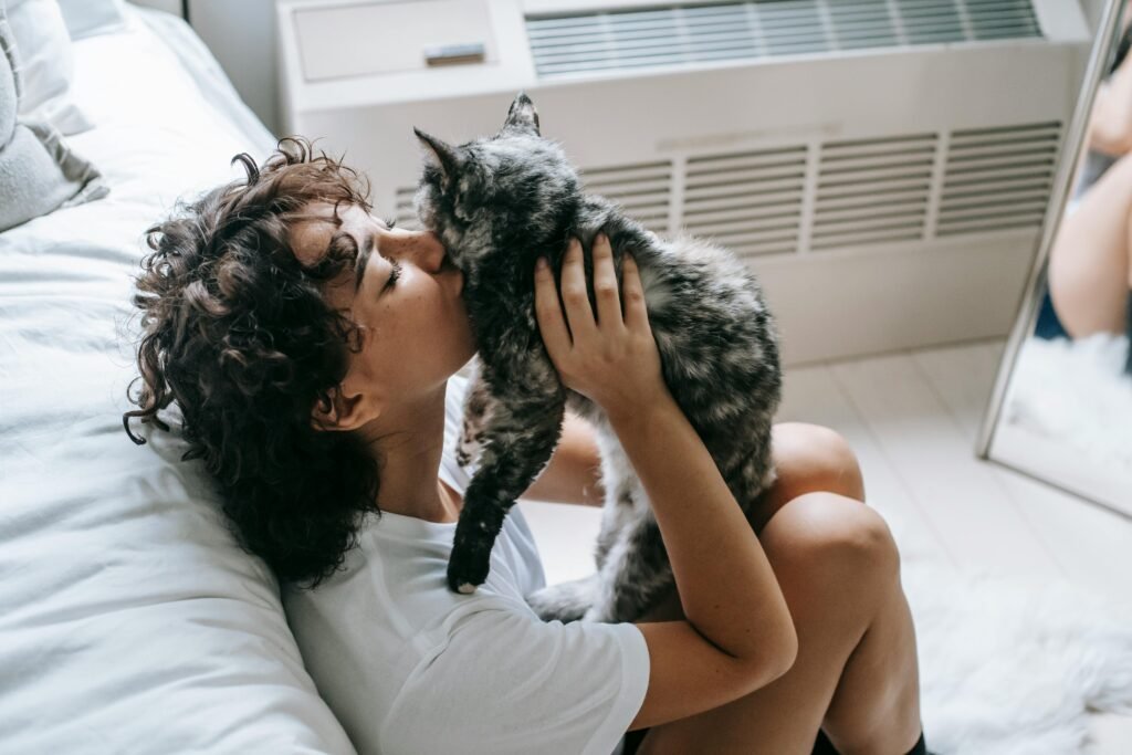 A woman lovingly kisses her cat in a cozy bedroom, showcasing warmth and affection.
