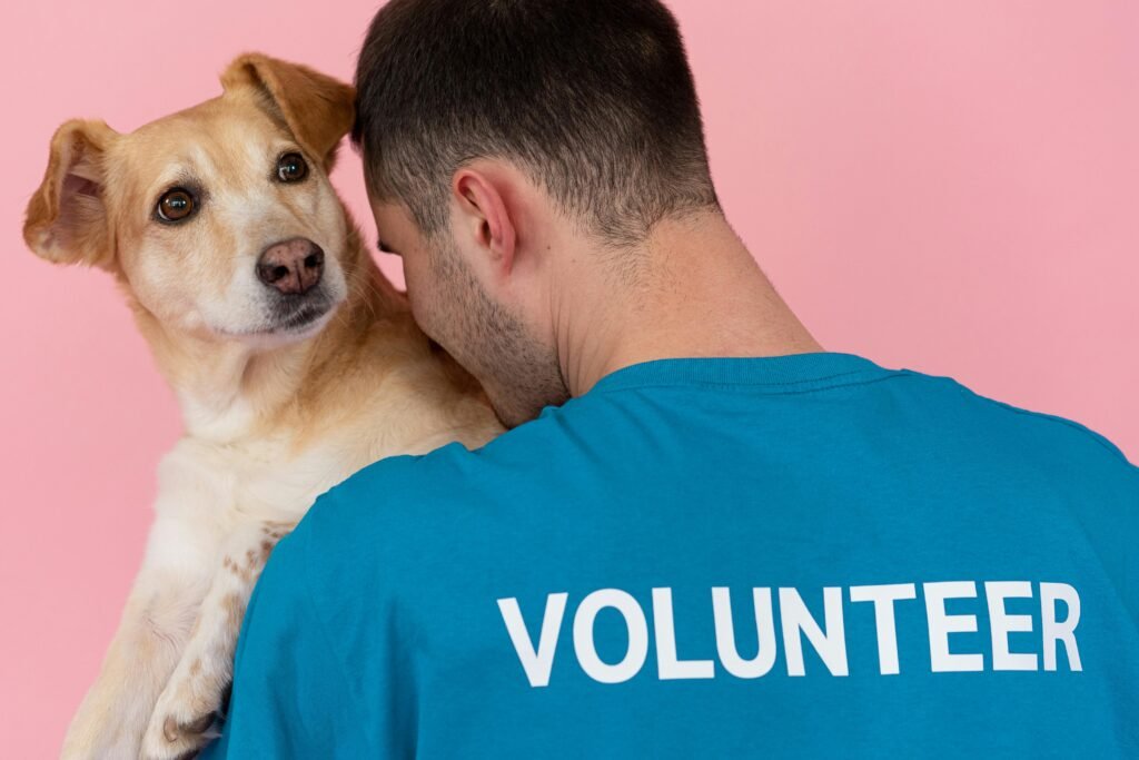 A volunteer holds a dog against a light pink background, showcasing community support and companionship.